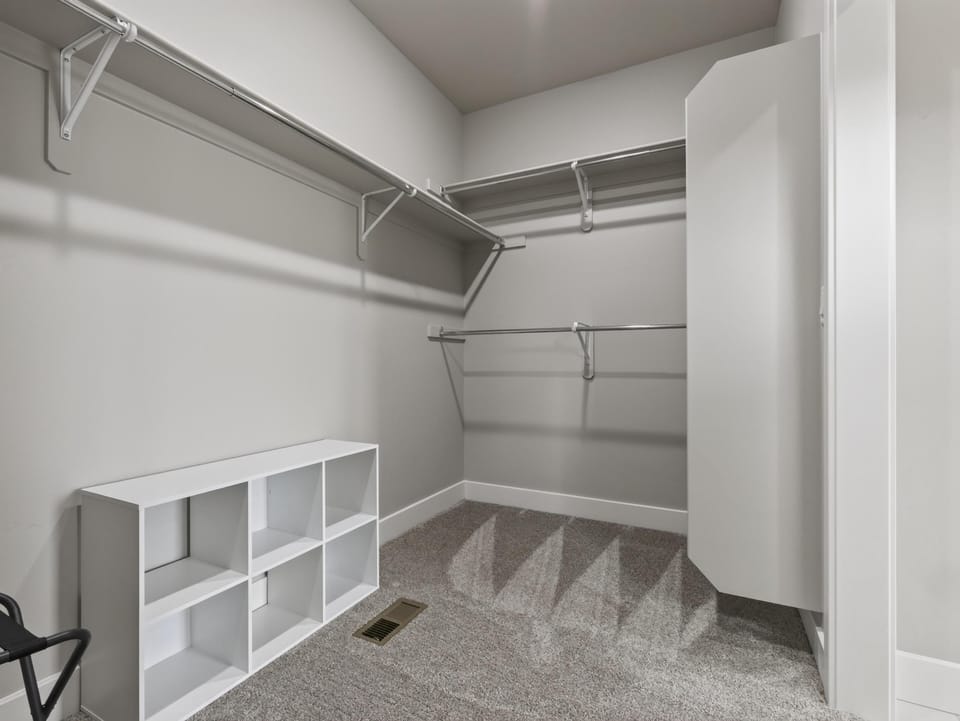 Closet features multiple hanging rods, a white cubby organizer, and plush gray carpeting underfoot.