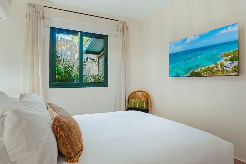 Rest beside a leafy garden view in this bright bedroom, complete with soft linens, warm accents, and natural light