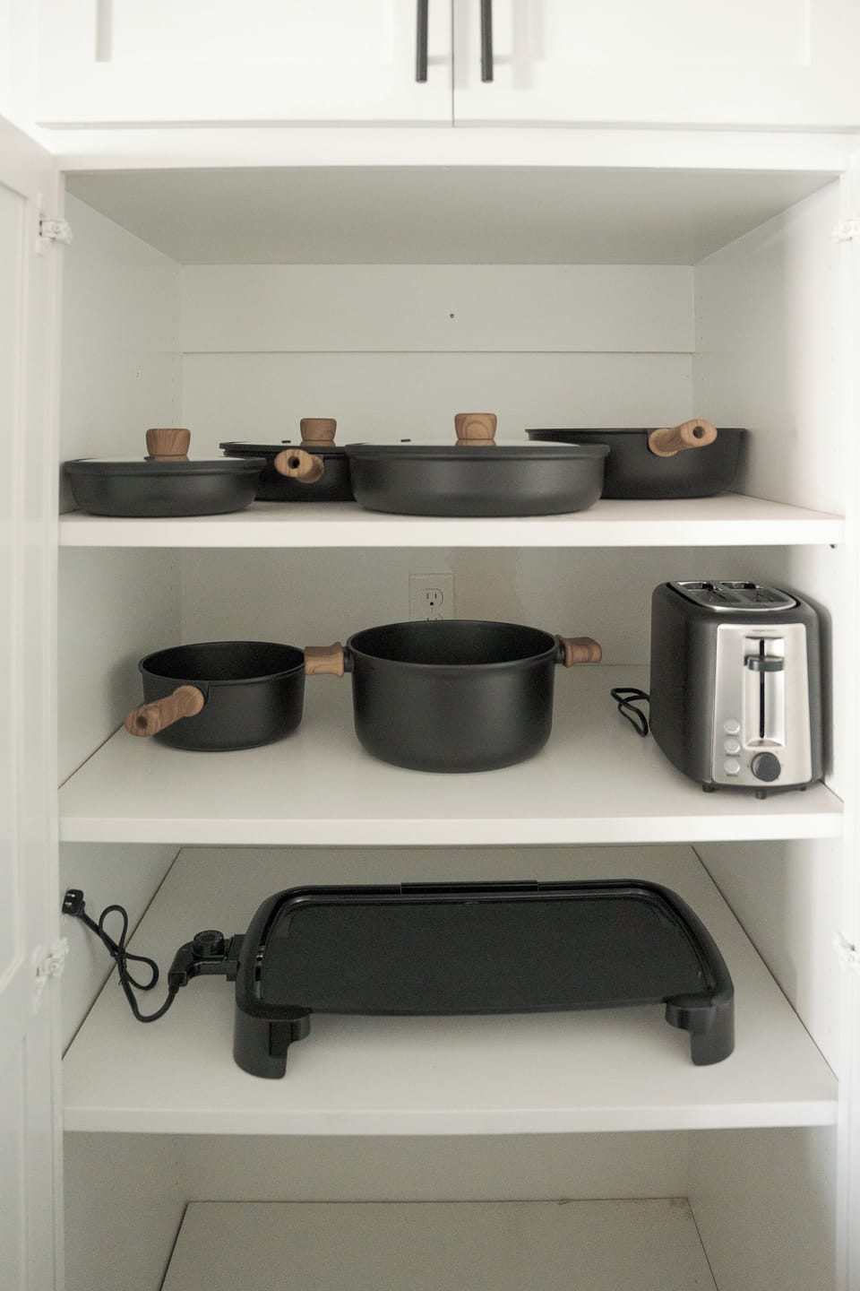Well-stocked kitchen cabinet with cookware, toaster, and griddle