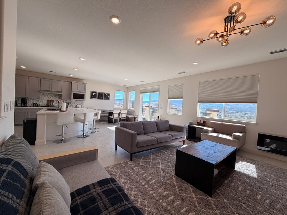 Unwind in this open, airy living area. Features large TV, comfortable seating, a modern fireplace, a sleek coffee table, yoga mat and large windows showcasing beautiful scenic views.