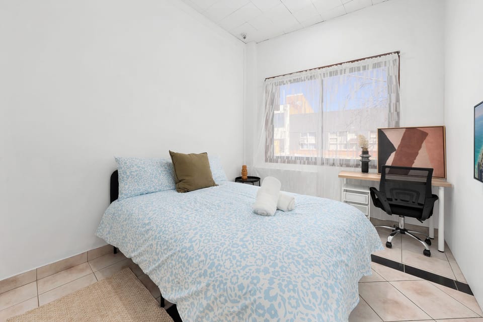 Bright bedroom with workspace, natural light, and cozy double bed