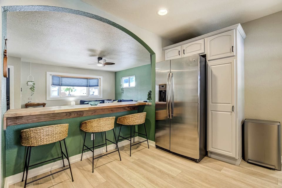 From the kitchen side, the bar becomes the natural gathering spot for coffee in the morning or a drink before dinner. Recessed lighting, a ceiling fan, and a stainless side by side refrigerator round out the working end.