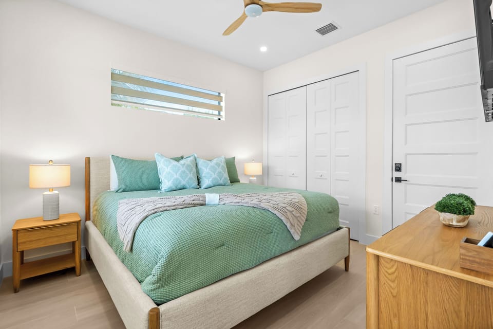 Serene bedroom with a green quilted bed, matching nightstands, ceiling fan, and clerestory window.