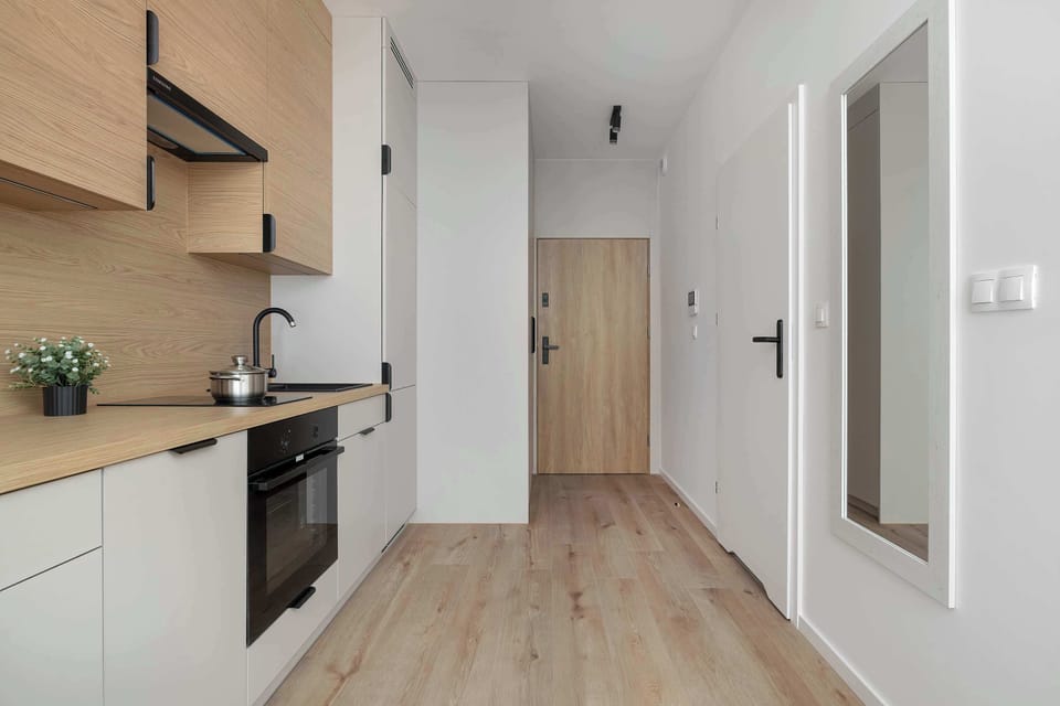 A hallway leading from the kitchen toward the apartment entrance, with built-in storage and warm wood flooring.