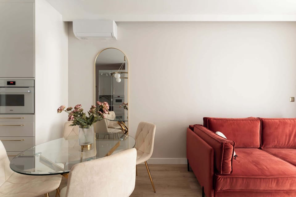 Stylowy salon z elegancką czerwoną sofą, efektownym kominkiem i telewizorem. Jasne wnętrze, naturalne światło oraz harmonijnie połączona strefa jadalniana tworzą przytulną i komfortową przestrzeń do wypoczynku.