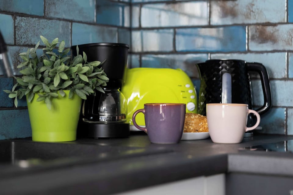A close-up view of the kitchen counter reveals a coffee maker, an electric kettle, a toaster, and colorful mugs.