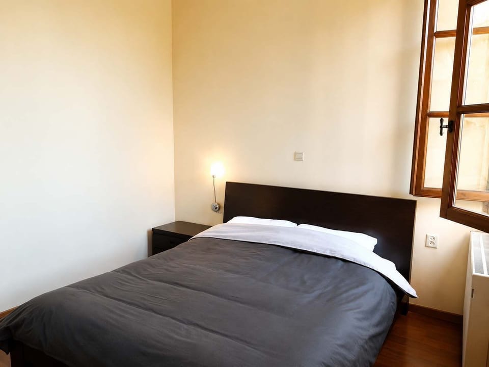 A peaceful double bedroom with simple furnishings, a wooden-framed window and soft bedside lighting