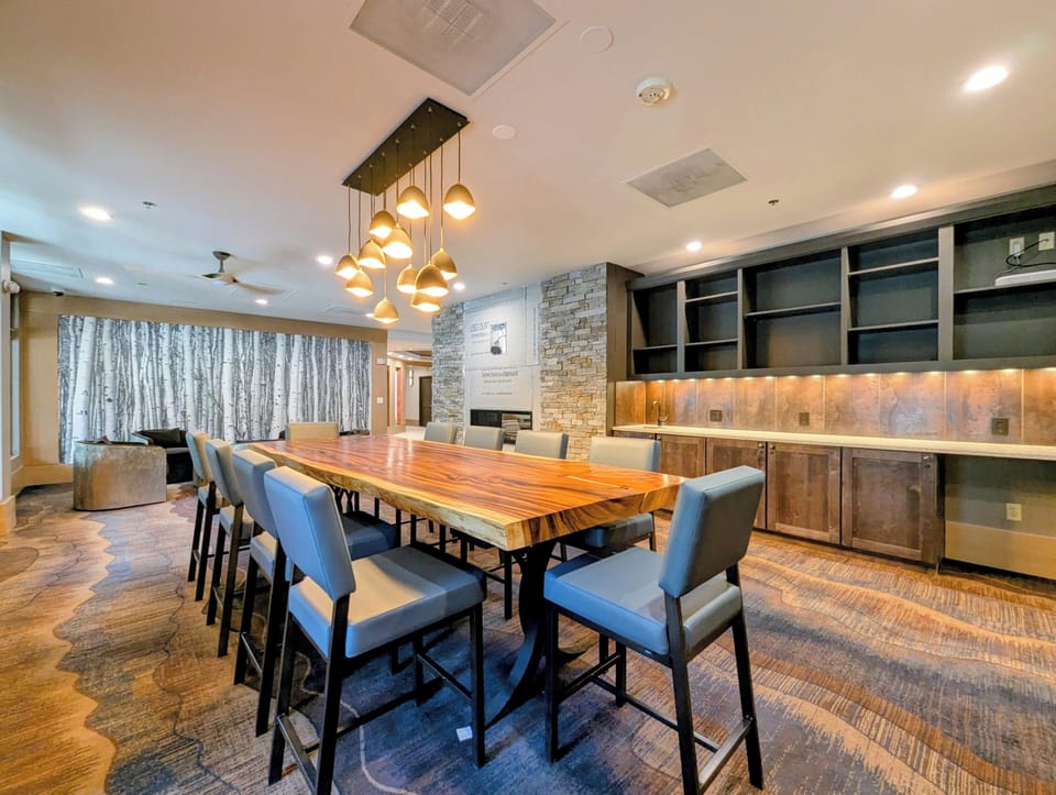 Gather around this stunning live-edge table beneath modern pendant lighting. The sleek kitchen, stone accents, and open flow into the lounge create an inviting space for memorable shared meals.