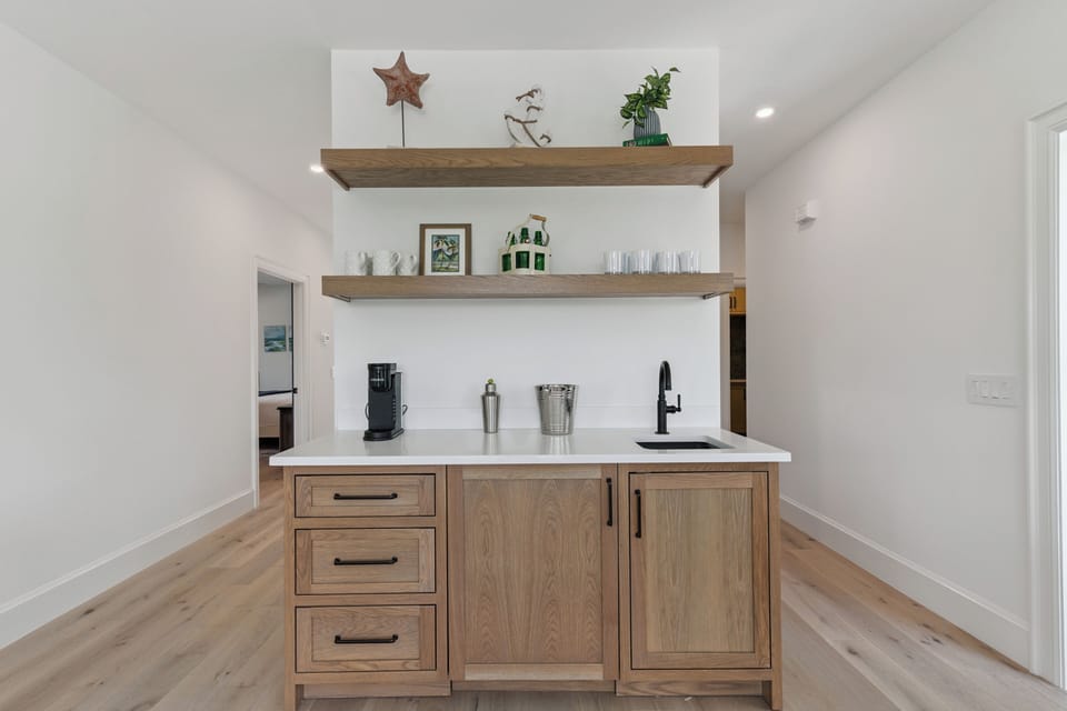 Your personal bar area awaits with a sleek countertop, mini-sink, and open shelving displaying glassware—perfect for mixing your favorite drinks in style.