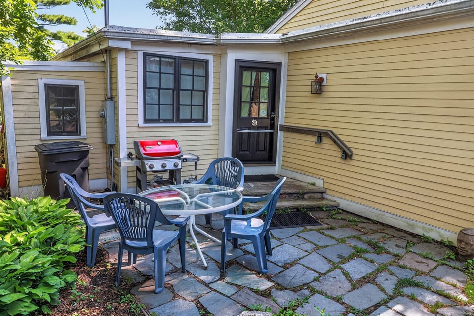Stone patio with an outdoor dining set and barbecue grill beside a yellow house.