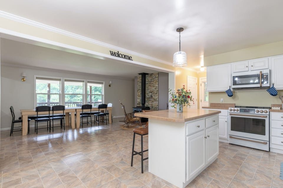 Bright open kitchen and dining space with island, big windows, and wood stove