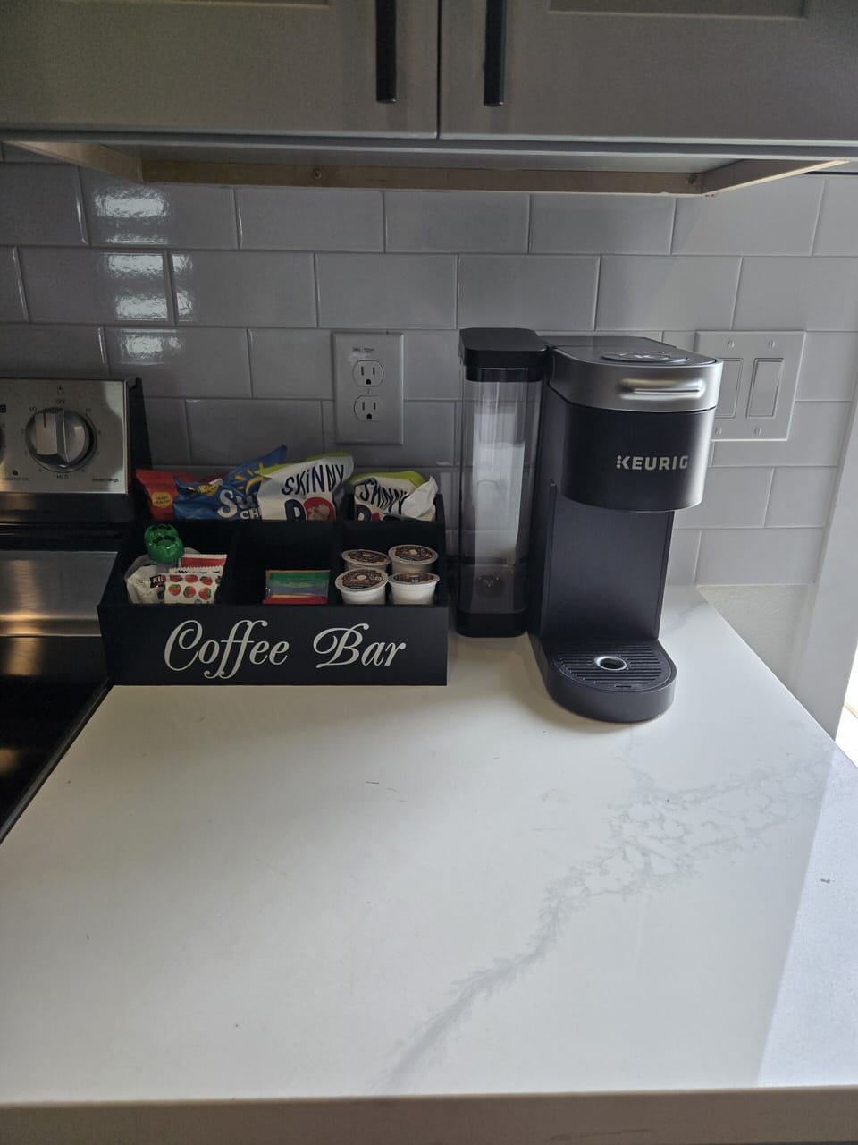 Modern kitchen coffee bar with Keurig, stocked pods, tea, and snacks