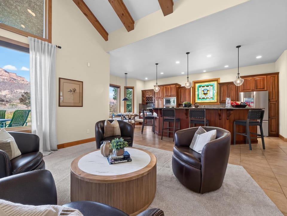 Four dark leather chairs circle a round marble-top coffee table on a beige rug near the kitchen bar.