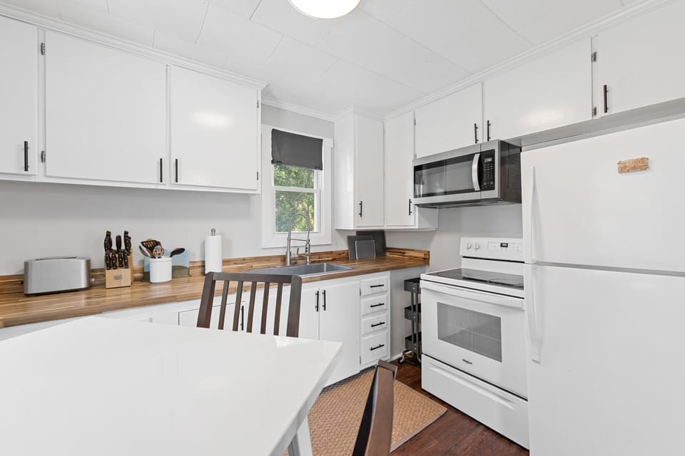 White cabinetry with black hardware surrounds a wood-grain countertop and stainless steel sink beneath a small window.