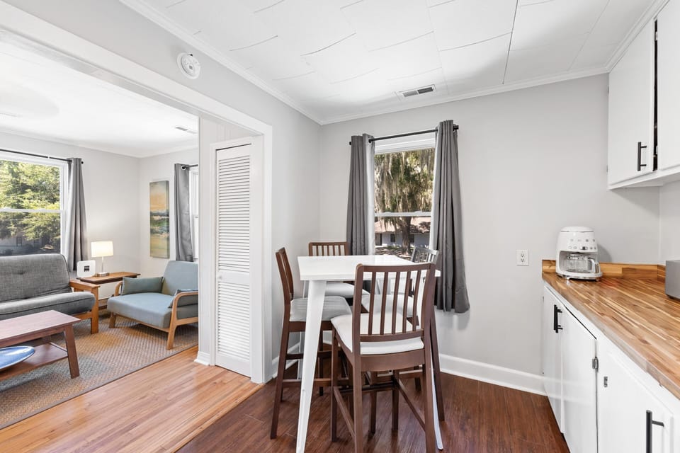Dining area with white high-top table and wooden chairs, adjacent to kitchen cabinets and wood countertop.