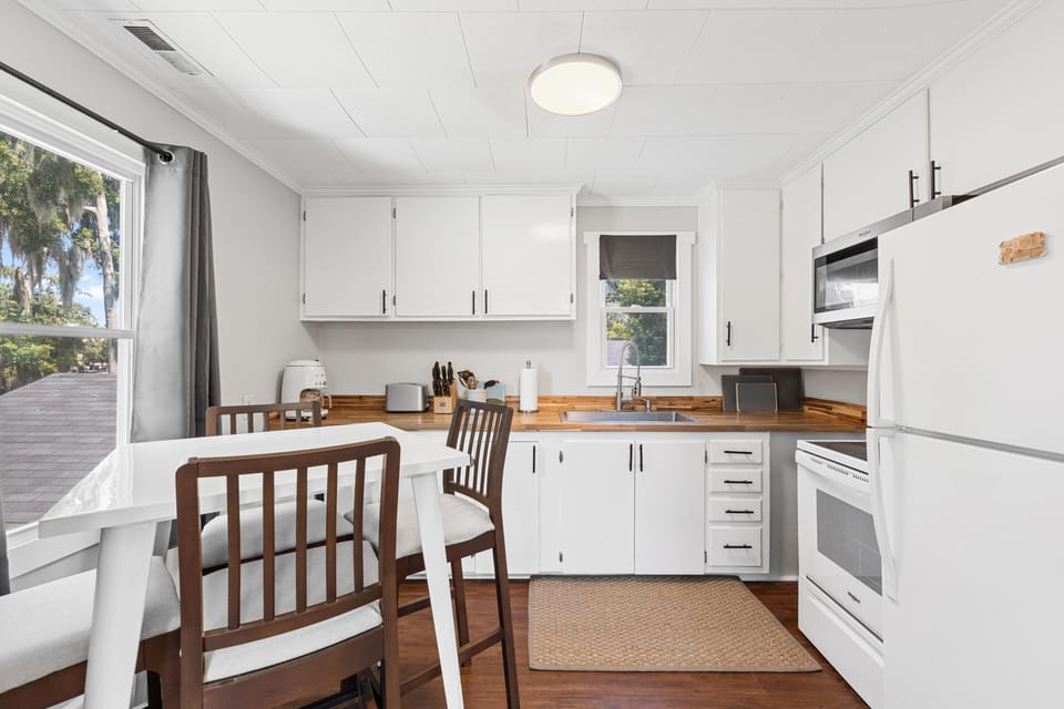 Dining table with cushioned wooden chairs faces white cabinetry and wood-grain countertops in the kitchen.
