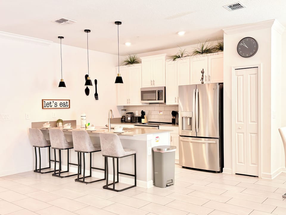 Gourmet white kitchen with quartz island, barstools, and pendants.