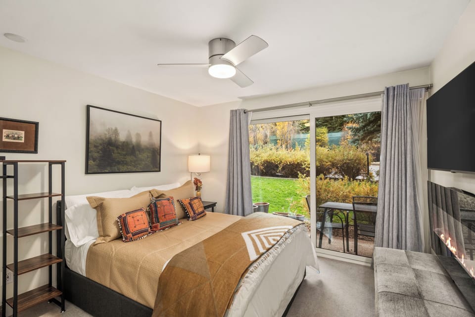 Bedroom with plush queen bed, smart TV, porch access, and detached bathroom. Please note the electric fireplace and bench has been replaced with a dresser for clothing storage.