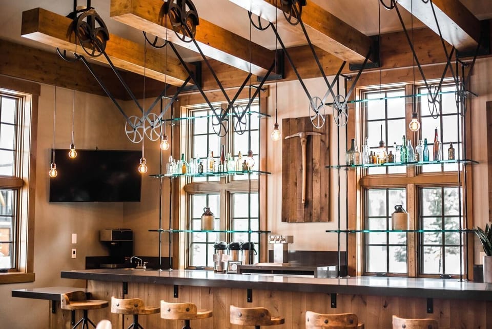 Rustic-industrial bar with exposed beams, bar seating, and bright windows