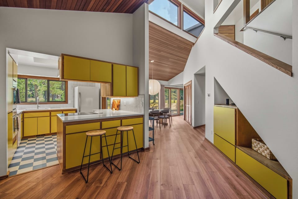 Light-filled retreat with soaring vaulted wood ceilings, clerestory windows, and rich hardwood floors. Bold yellow cabinetry brings warmth and cheer to the open-concept kitchen and dining area.