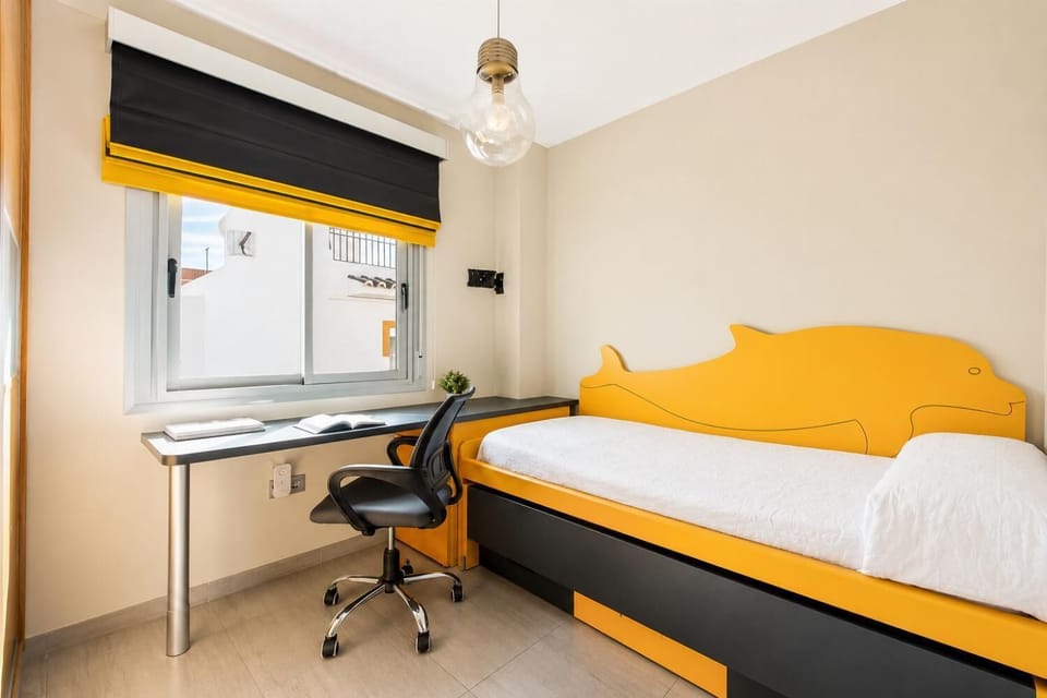 A vibrant modern bedroom features a yellow whale-shaped bed frame, a built-in study desk with an office chair, and a matching yellow and black window blind.
