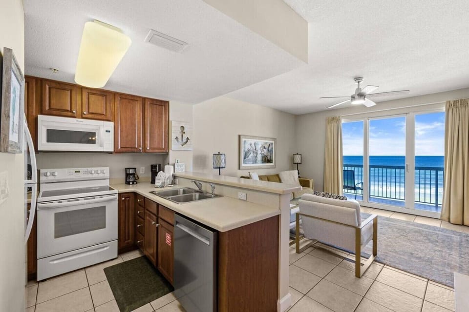 Cook and unwind in this open-concept condo featuring a full kitchen, comfortable seating, and bright Gulf views through sliding glass doors.