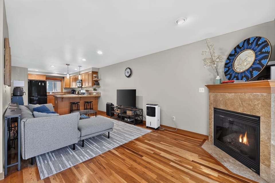 Cozy open living room with fireplace, hardwood floors, and breakfast bar