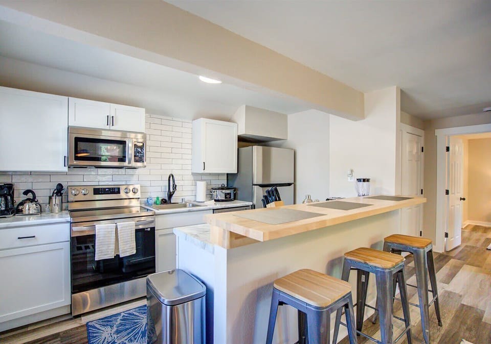 Modern kitchen with stainless steel appliances, subway tile backsplash, and a sleek breakfast bar with seating for three. Perfect spot for casual dining or enjoying morning coffee.