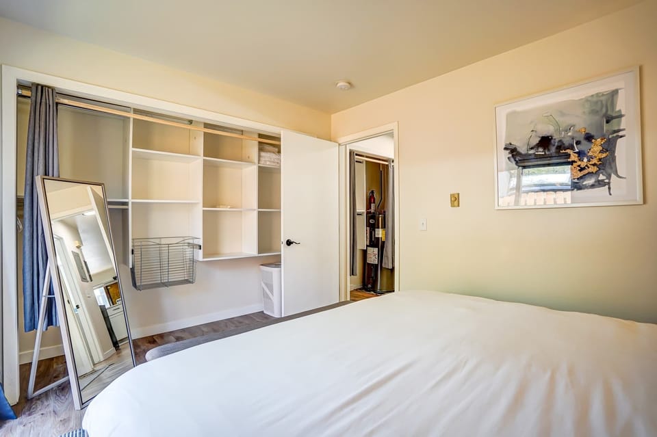 Bright and functional bedroom featuring an open closet system with shelving and a full-length mirror, providing ample space to unpack and settle in.