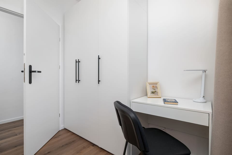 Functional bedroom workspace with a desk, chair, wardrobe, and large windows.