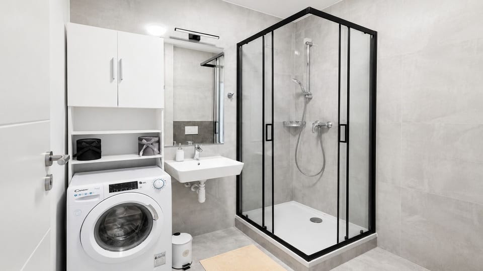 Modern bathroom with walk-in shower, laundry, and sleek finishes
