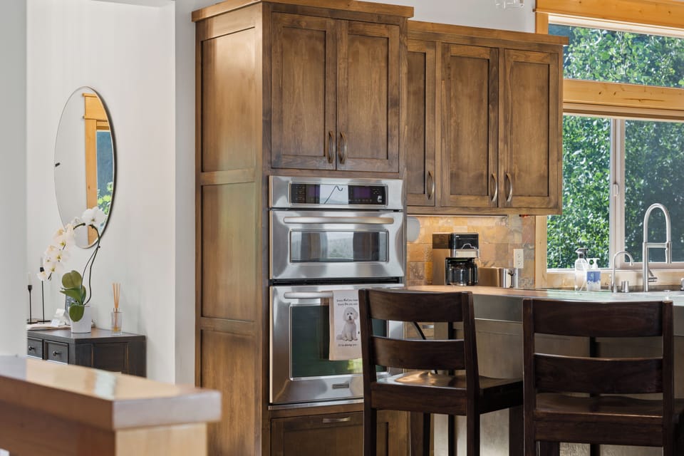 Gather around your fully-equipped kitchen, where rich wood cabinetry and modern stainless appliances make meal prep a breeze. Large windows frame lush greenery, bringing natural light into your vacation home.