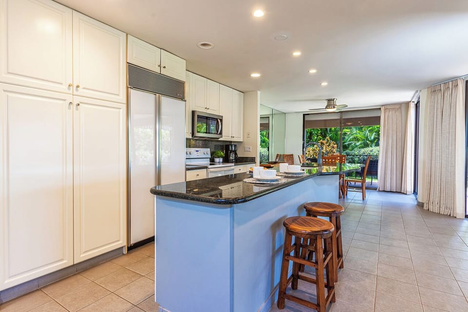 Step into your fully equipped kitchen with a spacious island and bar seating, opening to lush garden views that bring the outdoors in.