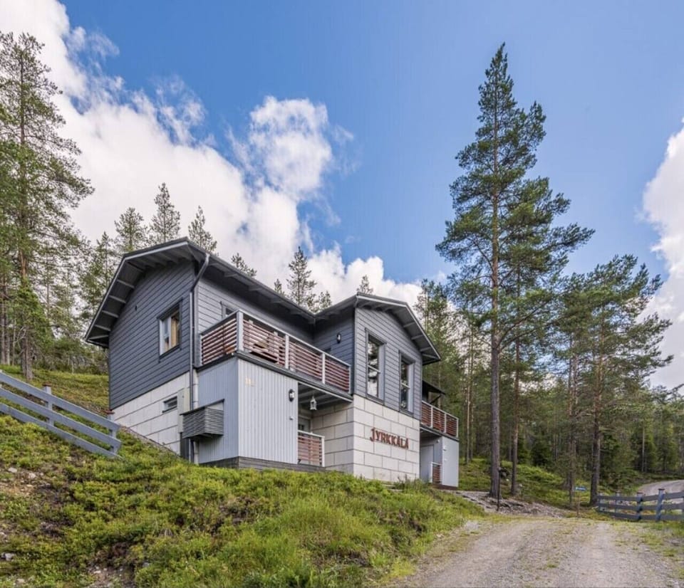 Exterior view of the two-story semi-detached property surrounded by pine forest in summer.