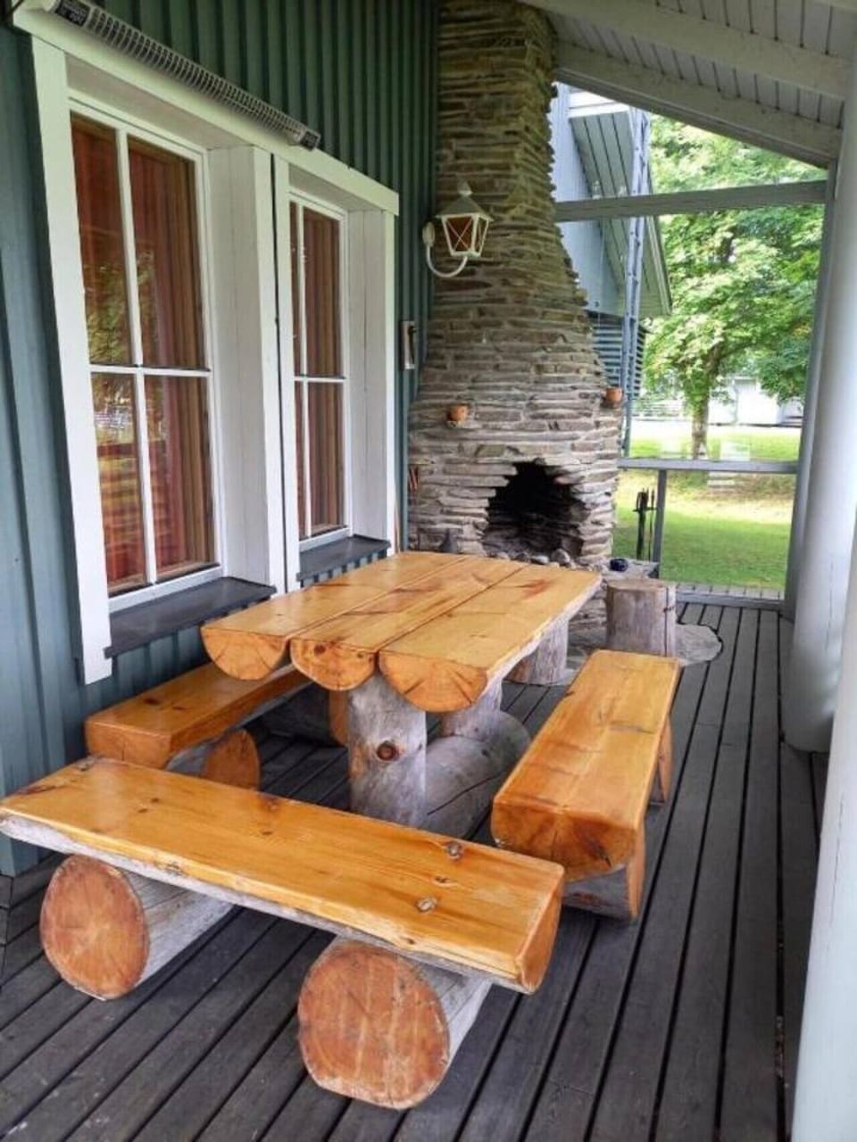 Glazed terrace with a stone fireplace and a large wooden table with benches.