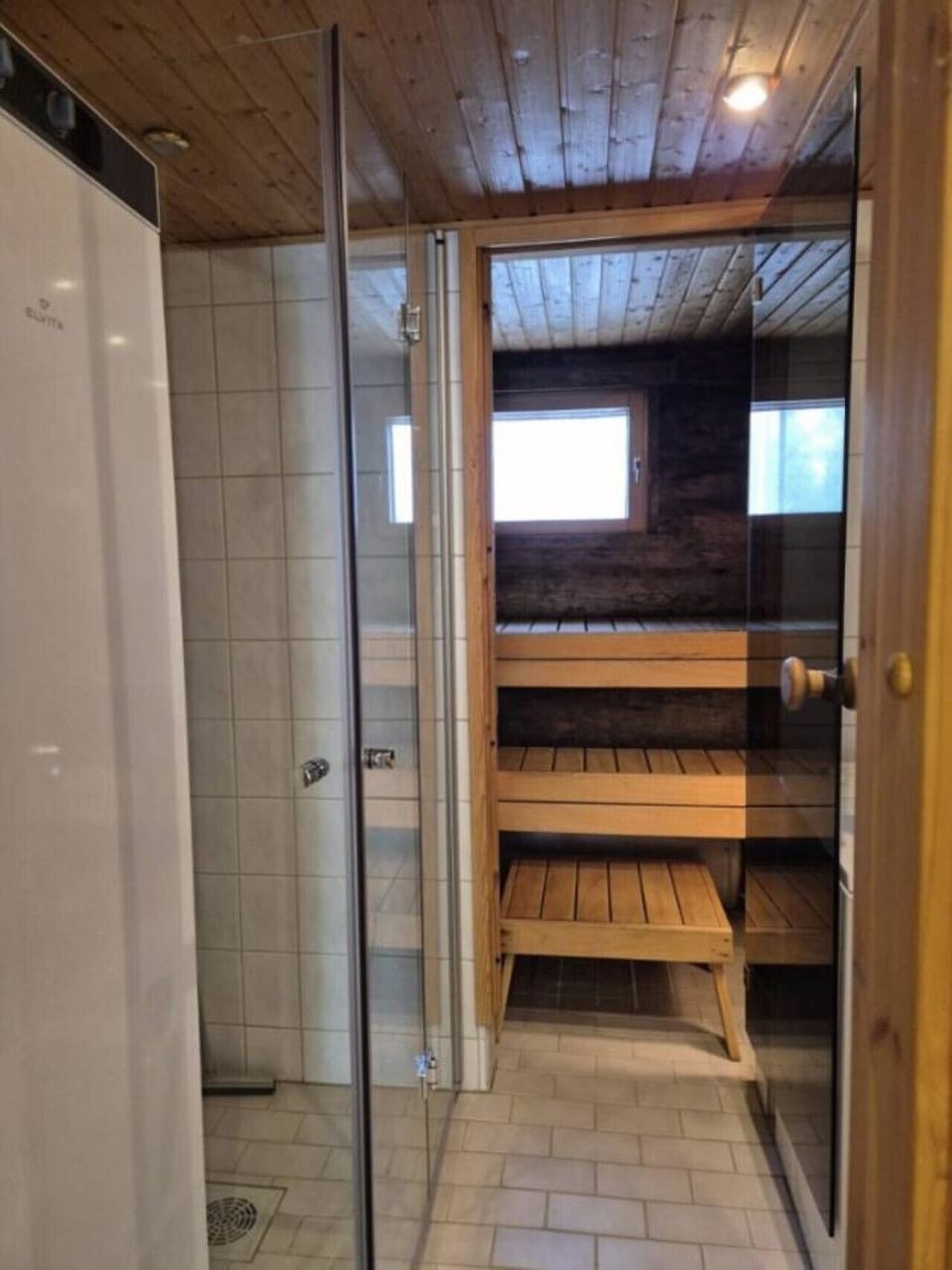Tiled shower room with a glass shower and a doorway through to the wooden sauna.