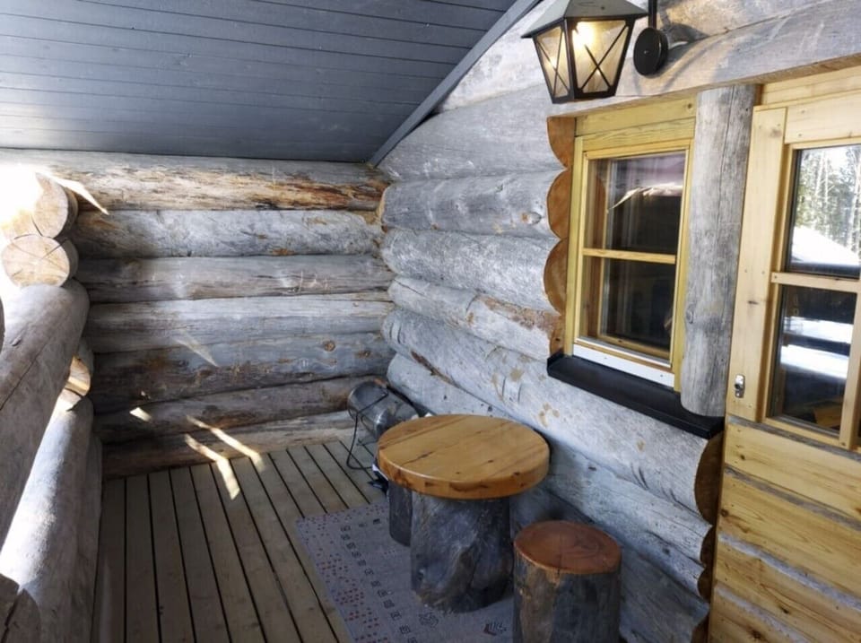 Sheltered porch with a round wooden table and log stools for sitting outside.
