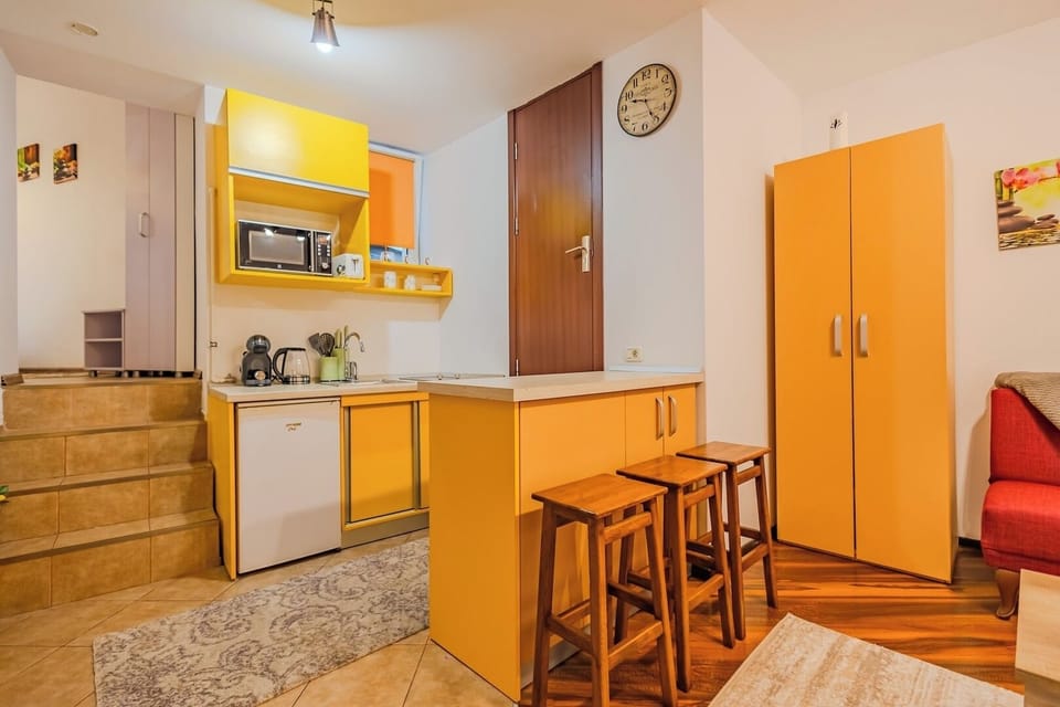 Full studio view with yellow kitchen, bar counter with 3 stools, mini fridge and entrance door. A compact, well-equipped self-catering space in the heart of Brasov's Old Town. Maia Studio, Brasov.