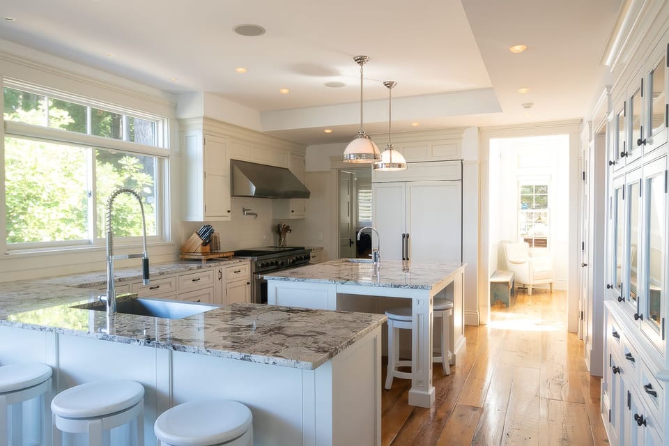 Bright luxury kitchen with dual islands, marble counters, and sunny dining nook