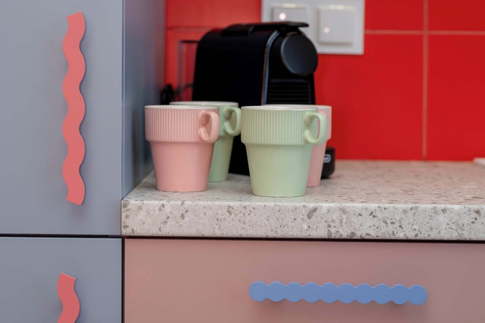 A close-up of colorful kitchenette appliances and mugs against a bright red backsplash.