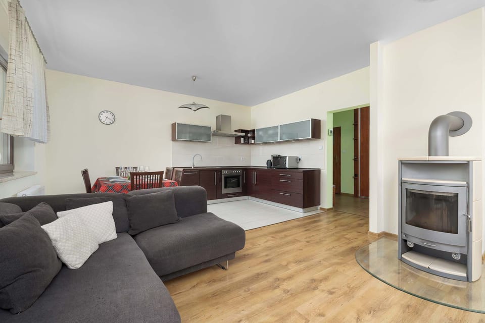 A wide-angle view captures the integrated living room, dining area, and open-plan kitchenette complete with a corner fireplace. The flowing floor plan allows seamless movement between cooking, dining, and relaxing spaces.