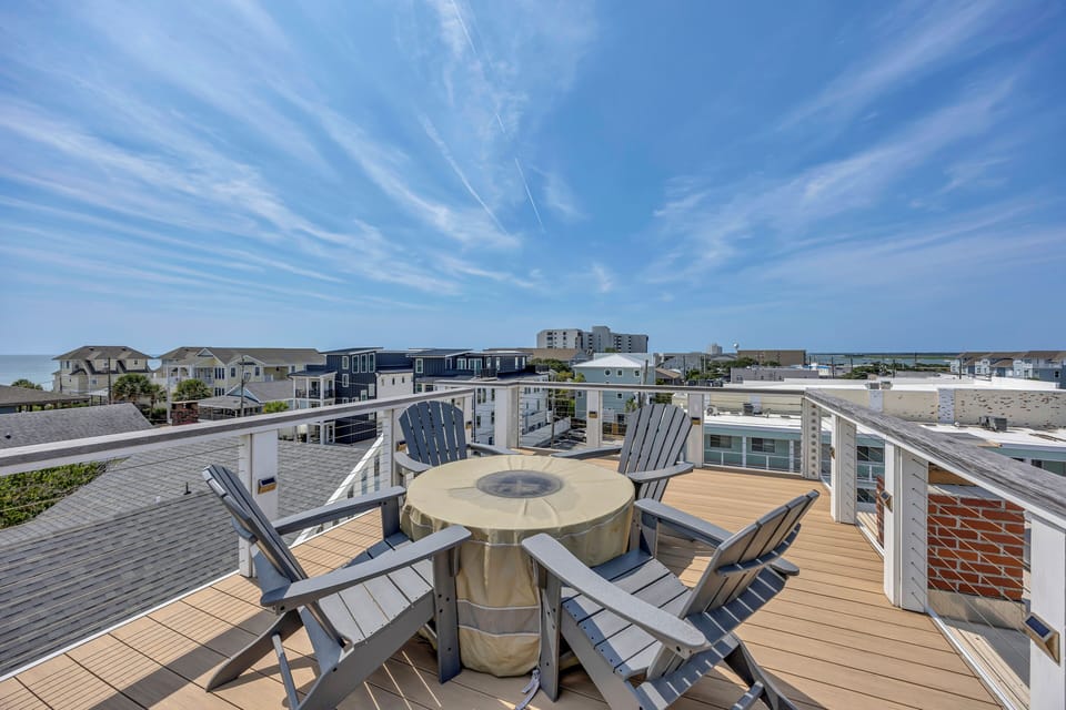 Rooftop terrace with sweeping coastal views, comfortable Adirondack seating, and a covered fire pit on warm wood decking. Perfect for morning coffee or evening relaxation with sea breezes and ocean views.