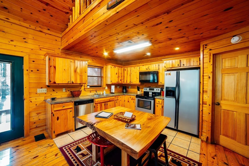 Gather around the rustic wood table in your fully equipped cabin kitchen, where gleaming stainless appliances meet cozy, knotty-pine charm. Everything you need to prepare delicious home-cooked meals awaits.
