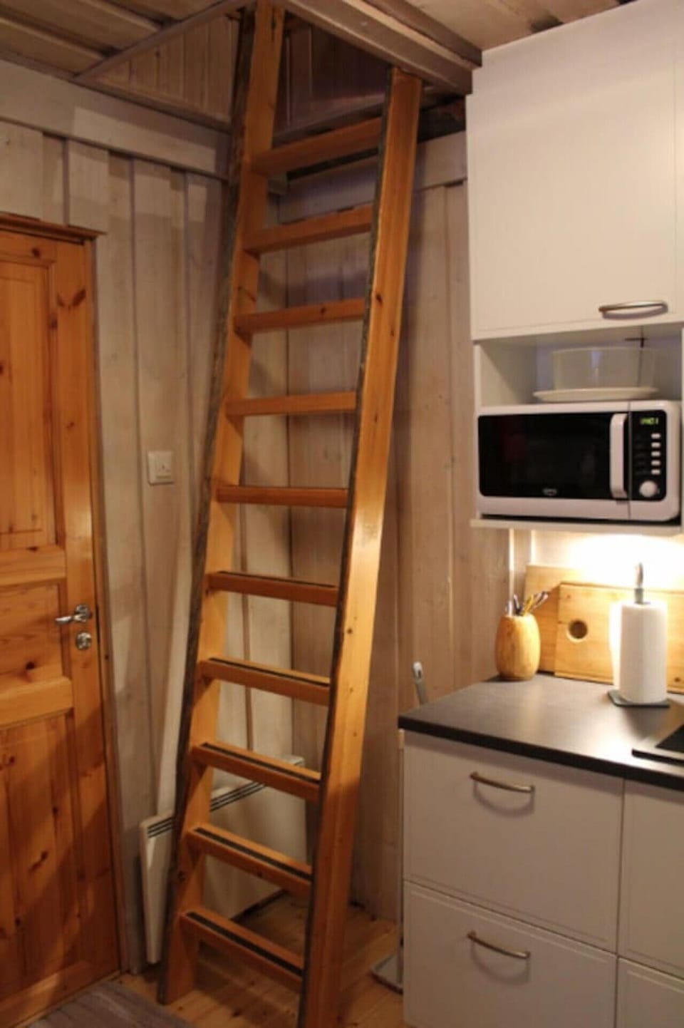 Steep wooden stairs to the loft beside the kitchen corner with a microwave.