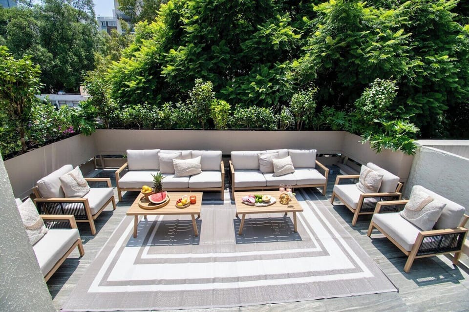 A spacious private terrace surrounded by lush greenery, with generous outdoor sofas and lounge chairs arranged for group gatherings. The open-air layout creates an inviting setting for conversations, drinks and relaxed evenings together.