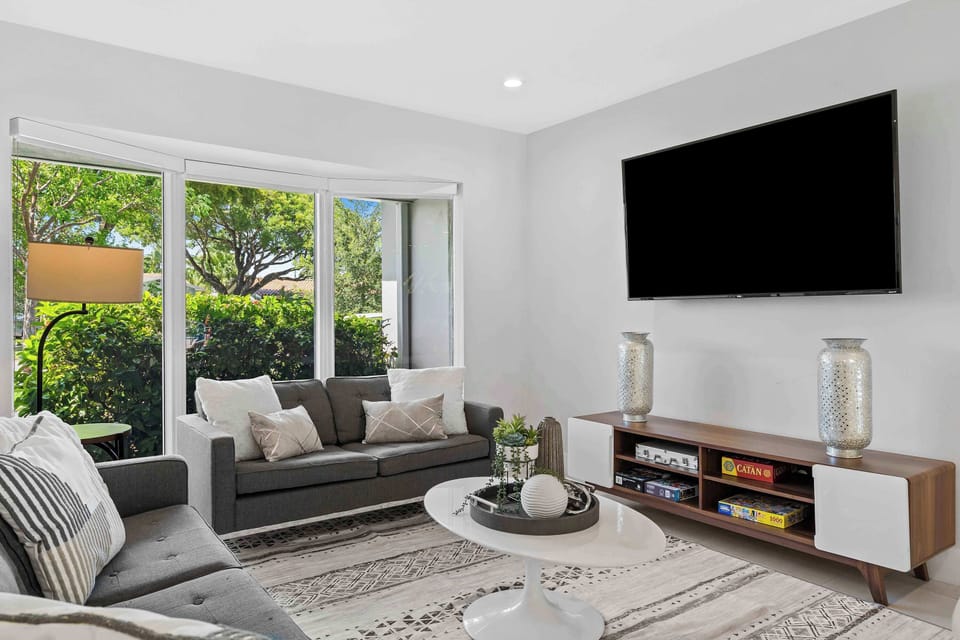 Bright open-concept interior featuring high ceilings, contemporary furnishings, a large TV lounge, and a formal dining setup.
