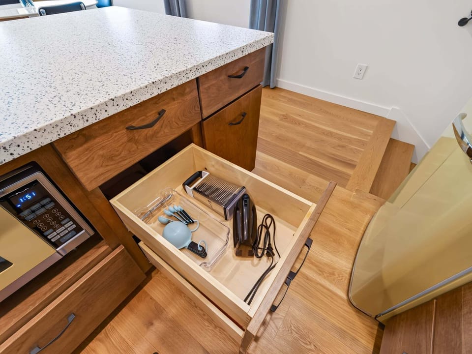 A retro-inspired kitchen with modern convenience, featuring warm wood cabinetry, vintage-style appliances, quartz countertops, and open shelving. Fully stocked with cookware, utensils, and everything you need to prepare meals with ease.
