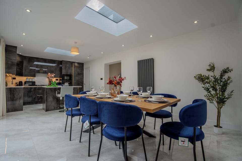 Open-Plan Kitchen & Dining Area: Gather around the stylish wooden table with vibrant blue velvet chairs, surrounded by s