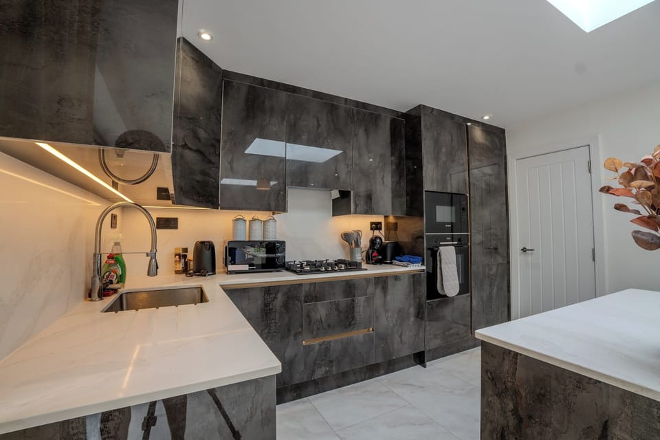 Kitchen Detail: Sophisticated cooking space with glossy dark cabinetry, white marble-effect worktops, and under-cabinet 