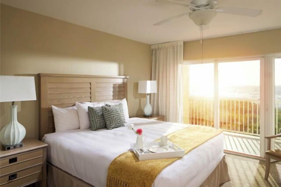Sunlit king bedroom with private balcony and serene outdoor views